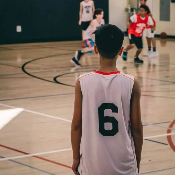 Barn som står på sidolinjer och tittar på spelare på basketplan